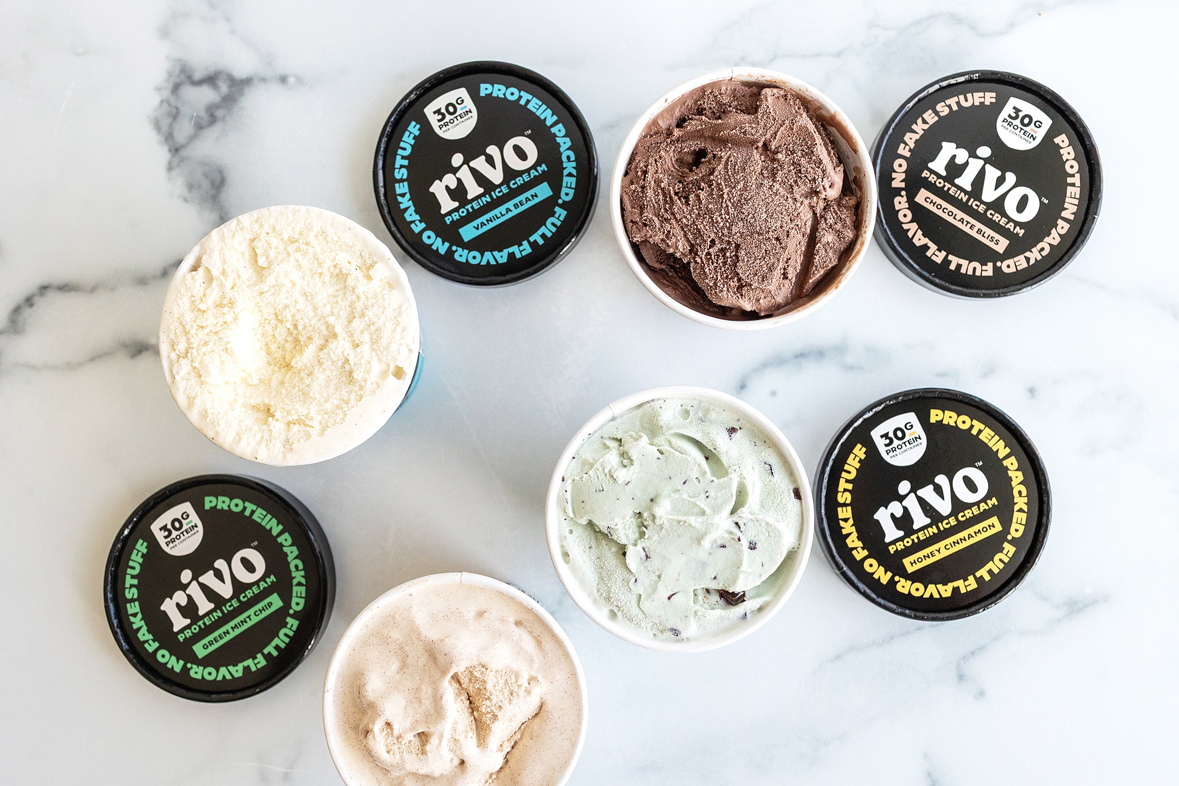 Assorted flavors of Rivo protein ice cream in containers on a marble surface