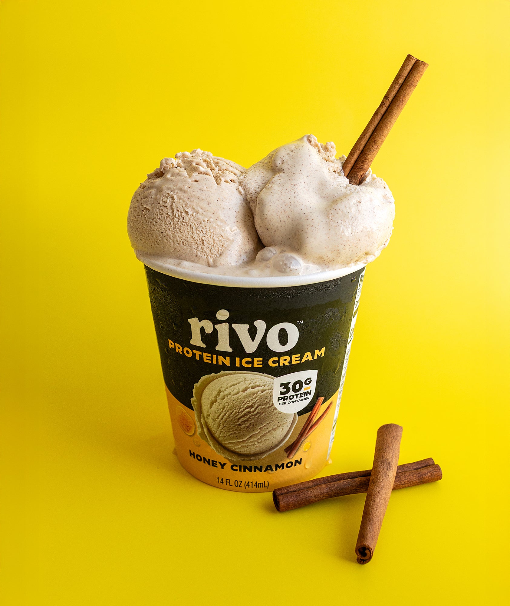 Rivo Protein Ice Cream container with honey cinnamon ice cream and cinnamon sticks on a yellow background
