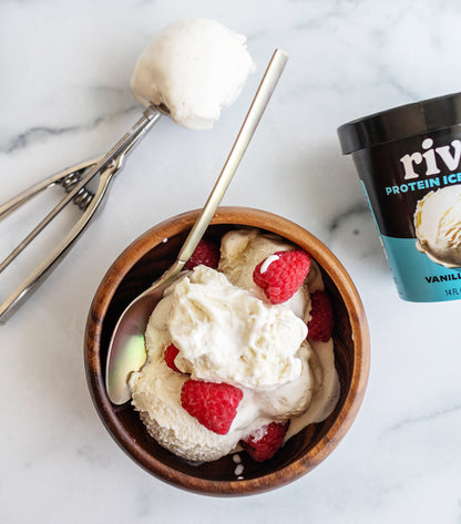 Bowl of RIvo vanilla bean ice cream with raspberries and a container of Rival Protein Ice Cream on a marble surface.