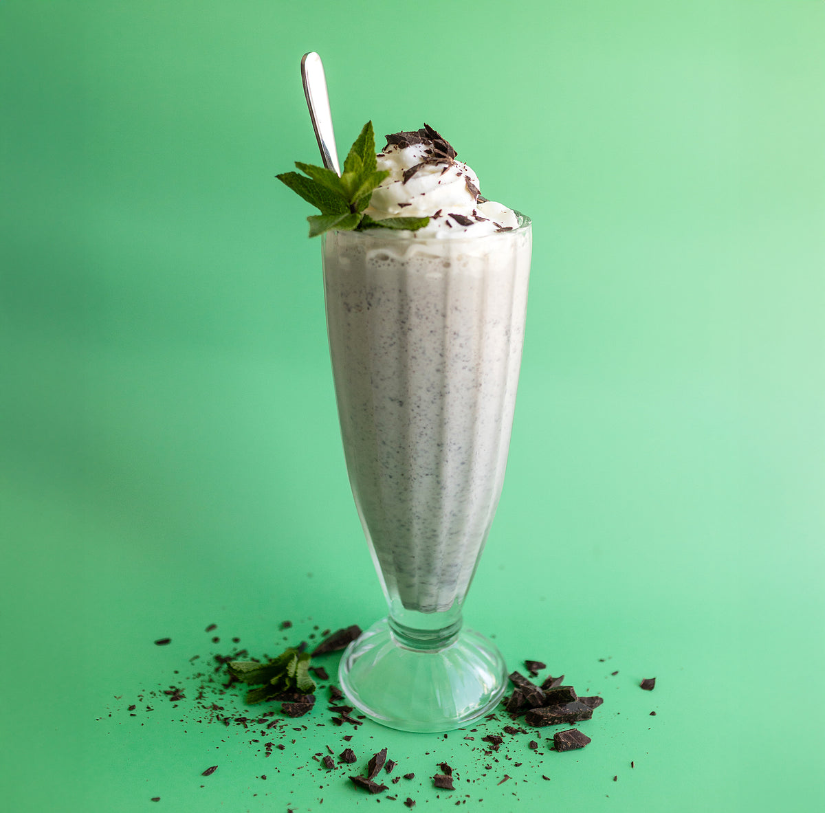 Mint chocolate chip shake made with Rivo protein ice cream with whipped cream and mint leaves on a green background