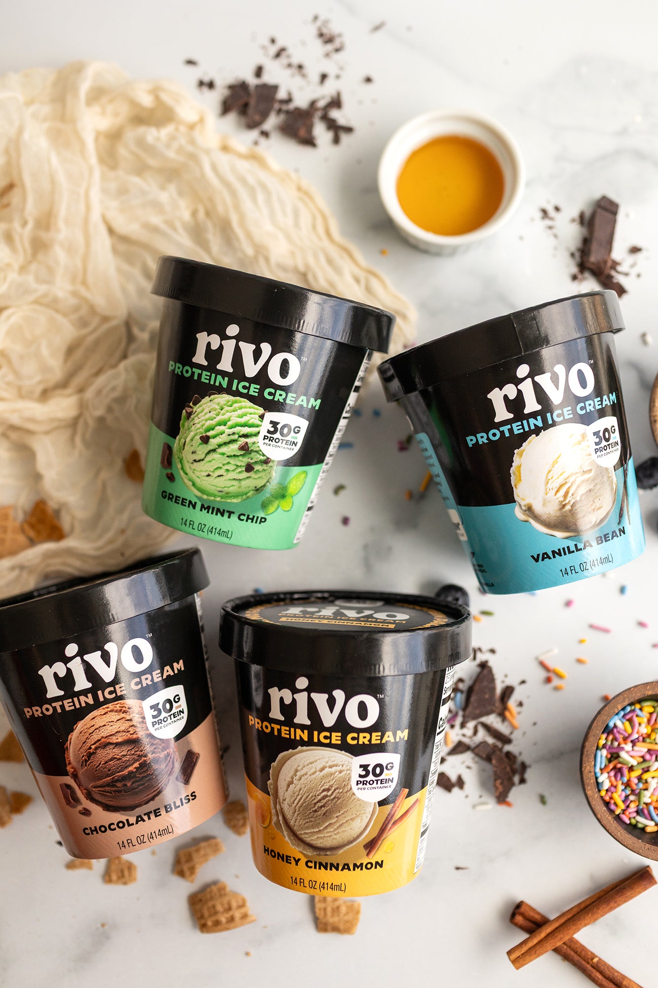 Four containers of Rivo protein ice cream on a white surface with ice cream and ingredients.