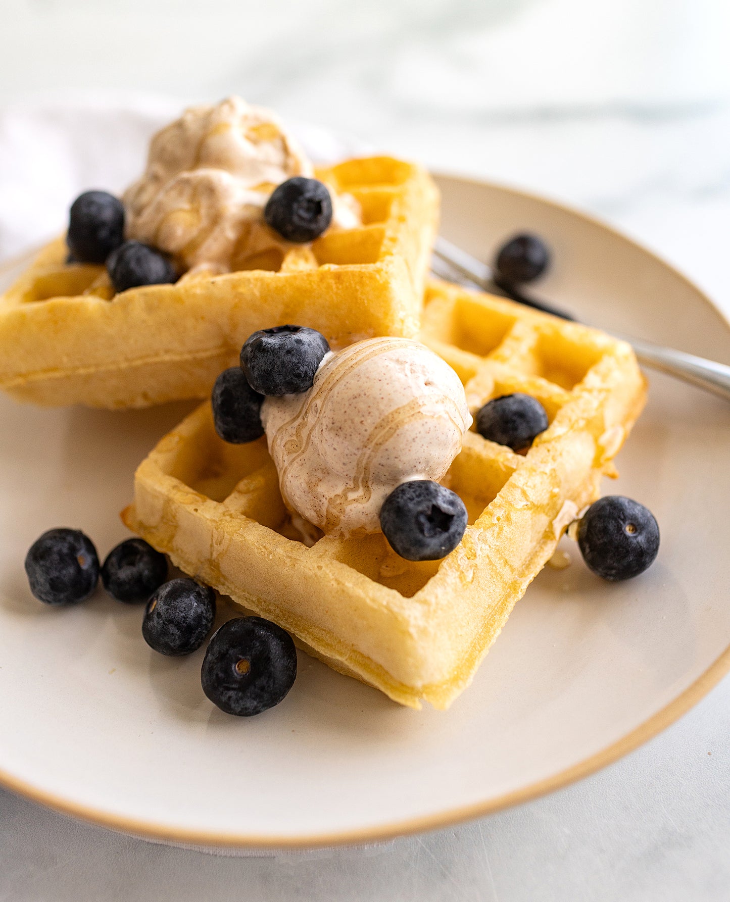 Waffles with blueberries and a scoop of Rivo honey cinnamon protein ice cream on a plate.